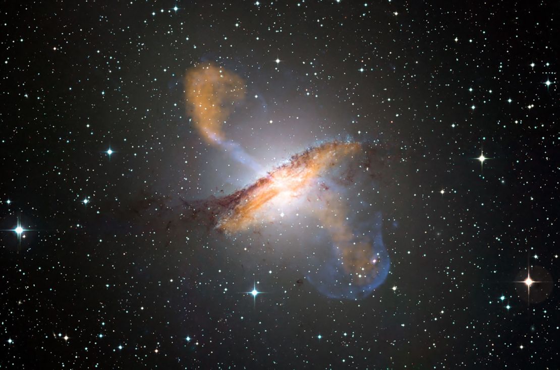 This composite image shows the Centaurus A galaxy in visible, microwave (orange) and X-ray (blue) light. Long jets expand out from the galaxy's central black hole on either side. 