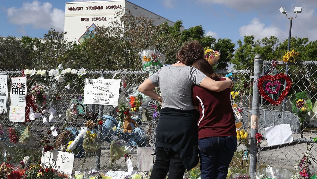 Margarita Lasalle, right, the budget keeper, and Joellen Berman, the guidance data specialist, look on at the memorial in front of Marjory Stoneman Douglas High School as teachers and staff are allowed to return to the school for the first time since the mass shooting on campus on February 23, 2018 in Parkland, Florida.