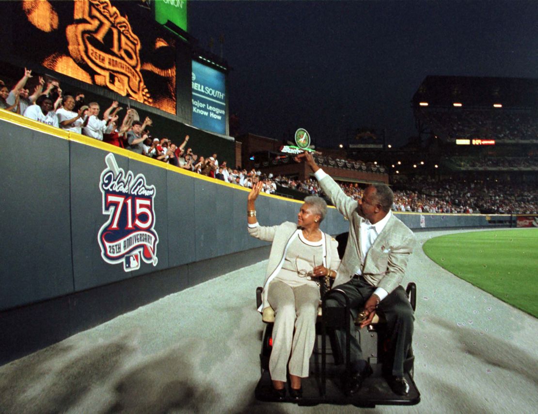 Aaron and his wife, Billye, wave to fans as they pass a sign honoring Aaron on the outfield wall at Turner Field after a ceremony honoring the 25th anniversary of Aaron's record-breaking home run.