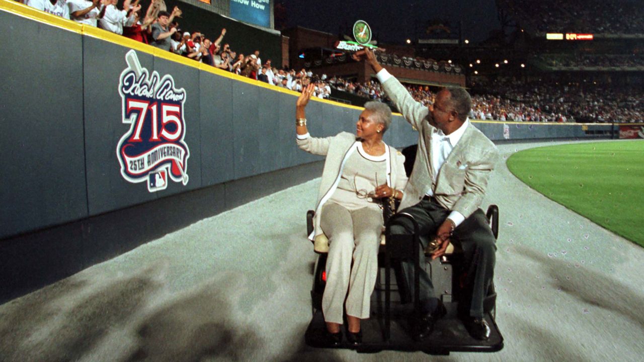 Aaron and his wife, Billye, wave to fans as they pass a sign honoring Aaron on the outfield wall at Turner Field after a ceremony honoring the 25th anniversary of Aaron's record-breaking home run.