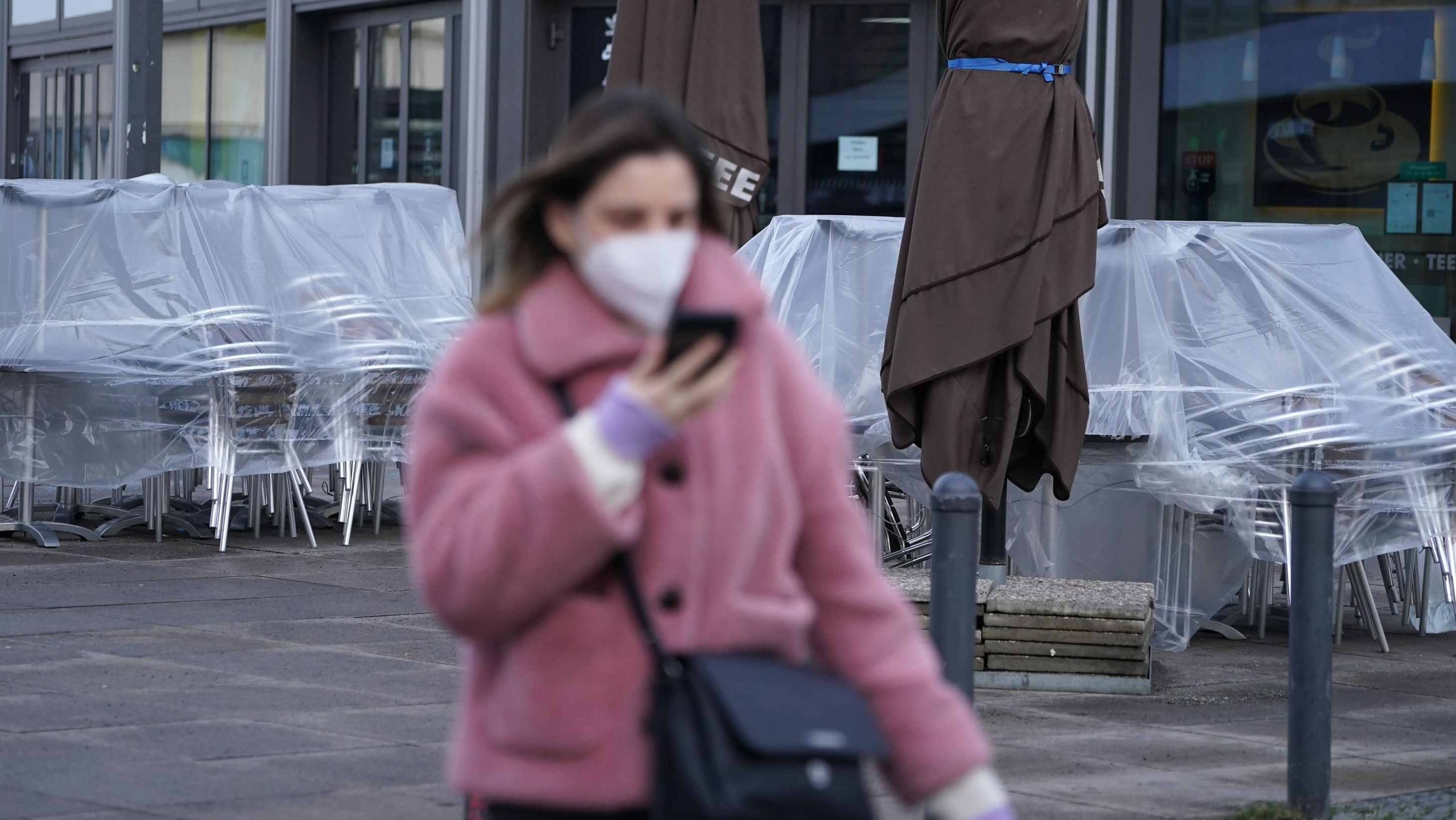 A woman wearing an FFP2 face mask walks past a shuttered cafe in Berlin, Germany.