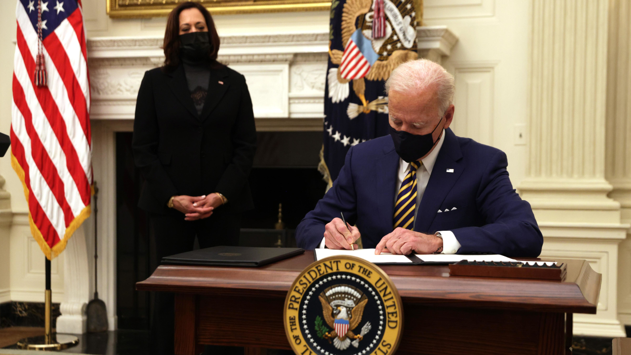 President Joe Biden signs an executive order as Vice President Kamala Harris looks on during an event on economic crisis, in the State Dining Room of the White House on January 22, 2021.