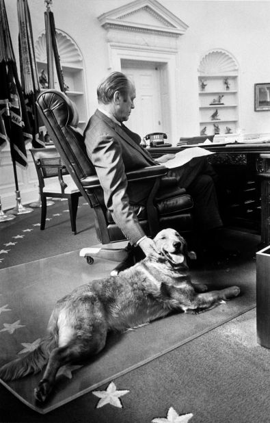 Gerald Ford pets his golden retriever, Liberty, while studying budget matters in the Oval Office.