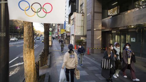 People wearing face masks walk and ride past an Olympics decoration installed along a street in Tokyo on Thursday, January 21.