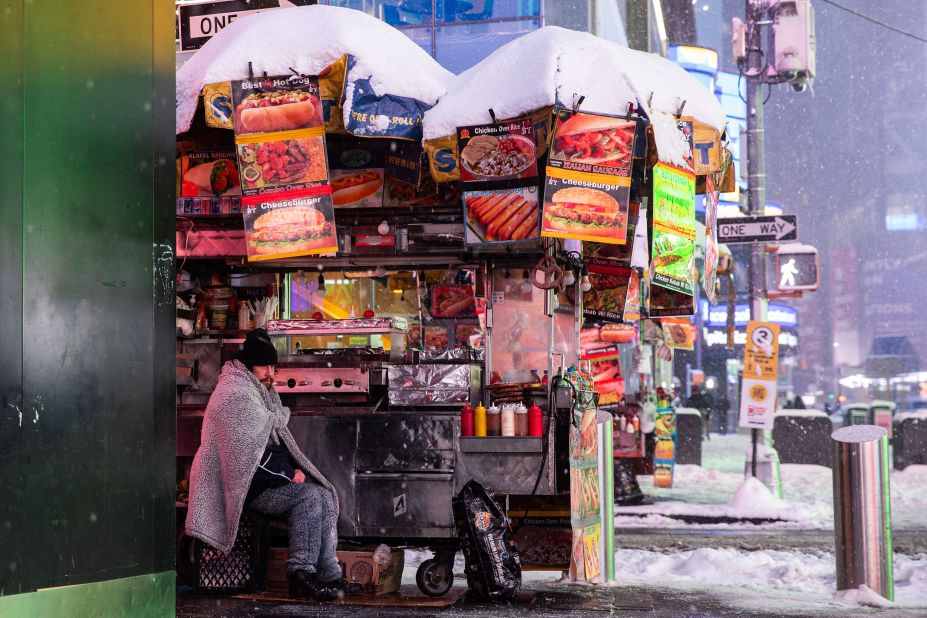 A food-cart vendor is wrapped in a blanket as snow falls in Times Square on Monday.