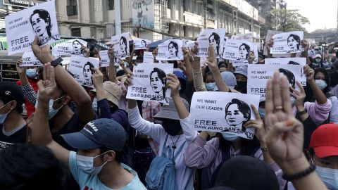 Demonstrators hold placards showing the image of Aung San Suu Kyi as they flash the three-finger salute in Yangon on February 7, 2021.