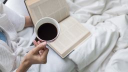 Woman on the bed with a book and cup of coffee.