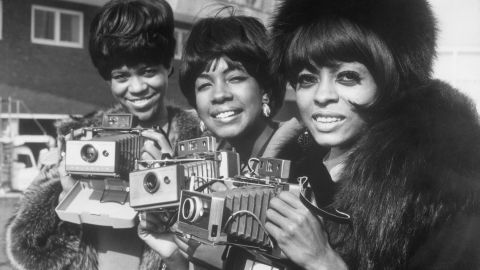 The Supremes (left to right, Florence Ballard, Mary Wilson, and Diana Ross) pose with their cameras as they arrive at London Airport.