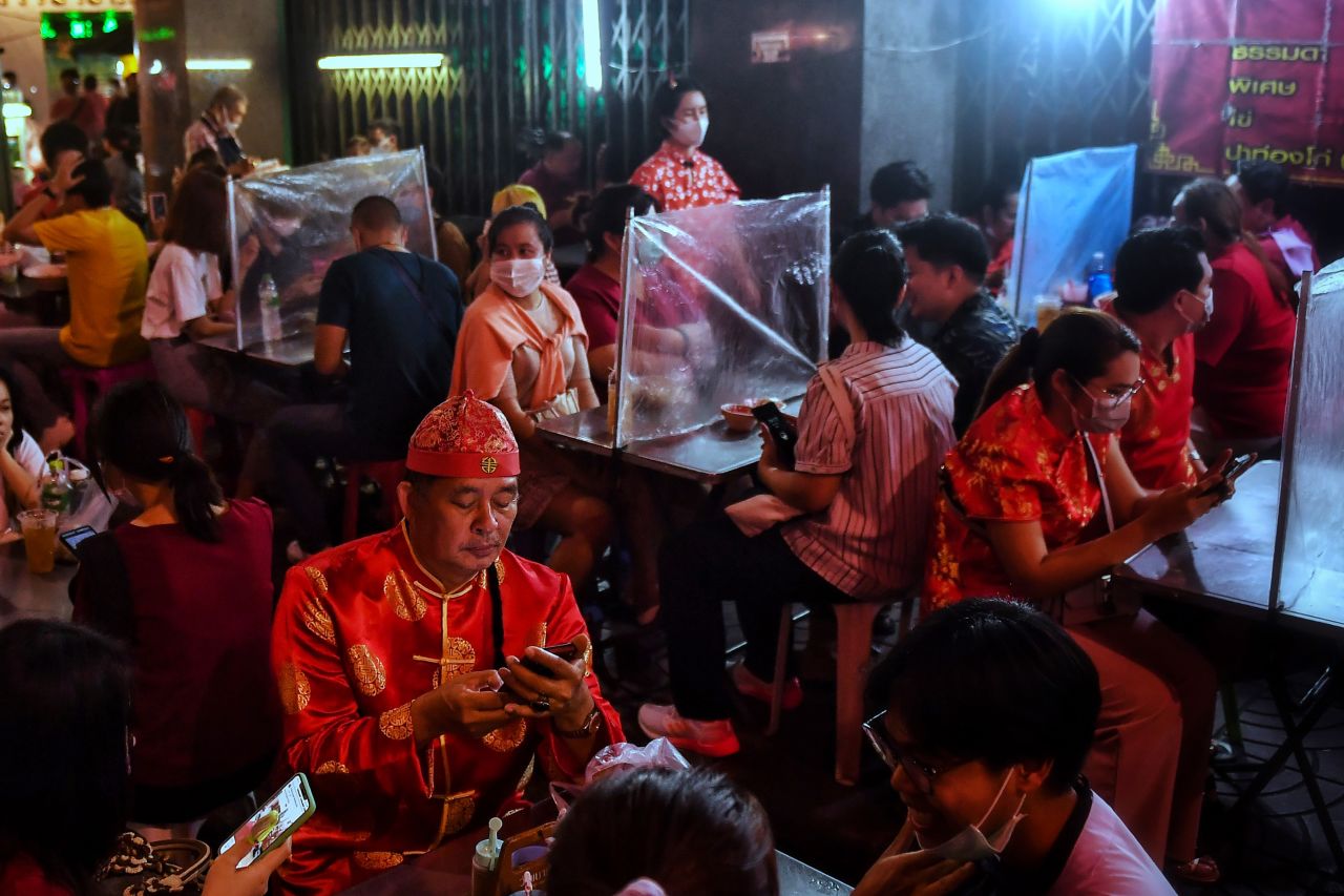 A man wearing a traditional Chinese outfit uses his cell phone as he waits for his meal in Bangkok's Chinatown.
