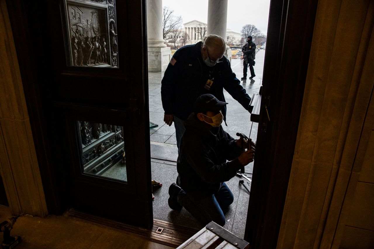 Workers replace window panes on Capitol doors that were damaged in last month's riot.