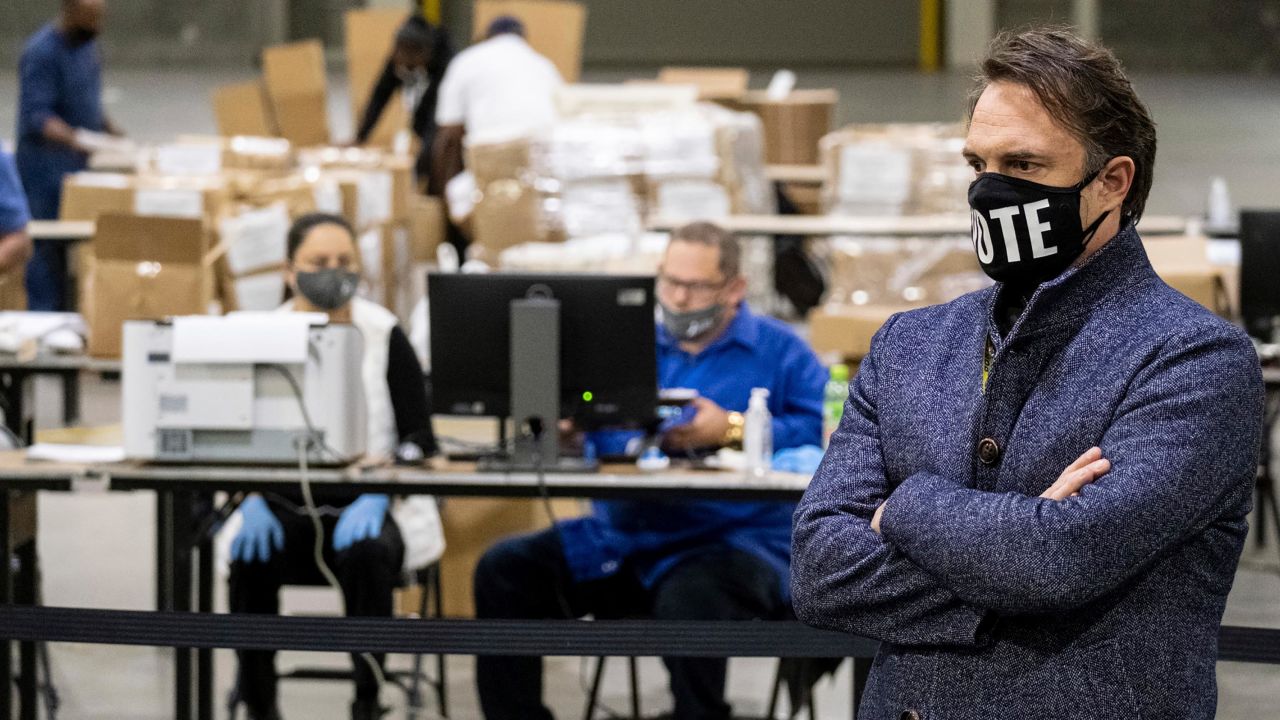In this November 25, 2020, file photo, Fulton County, Georgia, election chief Richard Barron listens to a question during a news conference while workers scan ballots behind him as the presidential recount gets underway at the Georgia World Congress Center in Atlanta.  