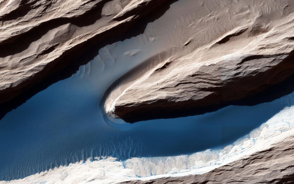 Although Mars isn't geologically active like Earth, surface features have been heavily shaped by wind. Wind-carved features such as these, called yardangs, are common on the red planet. On the sand, the wind forms ripples and small dunes. In Mars' thin atmosphere, light is not scattered much, so the shadows cast by the yardangs are sharp and dark.