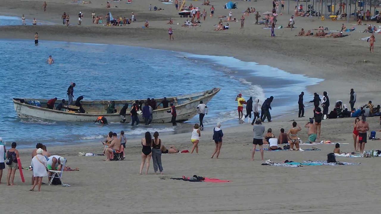 Refugees in an open boat land between sunbathing tourists on the beach at Los Cristianos, on December 10, 2020. 