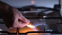 A man lights a gas stove with a match