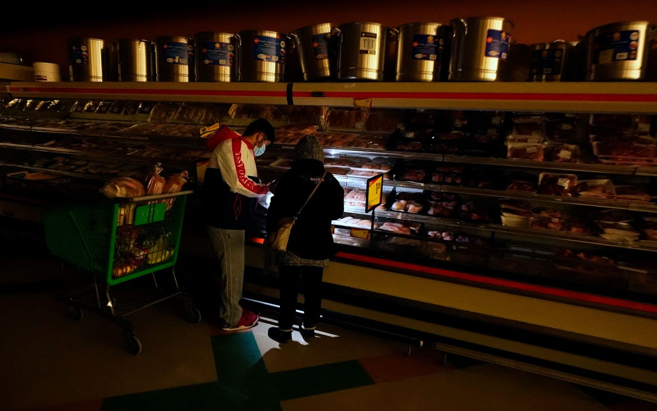Customers use light from a cell phone as they shop for meat at a grocery store in Dallas on Tuesday. Even though the store lost power, it was open for cash-only sales.