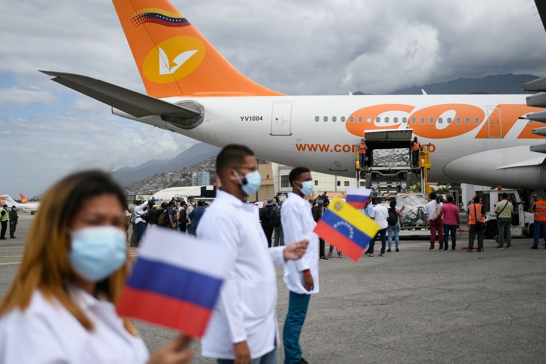 Healthcare workers hold national flags from Venezuela and Russia as workers unload a shipment of the Russian COVID-19 vaccine Sputnik V, at the Simon Bolivar International Airport in Maiquetia, Venezuela, Saturday, Feb. 13, 2021.
