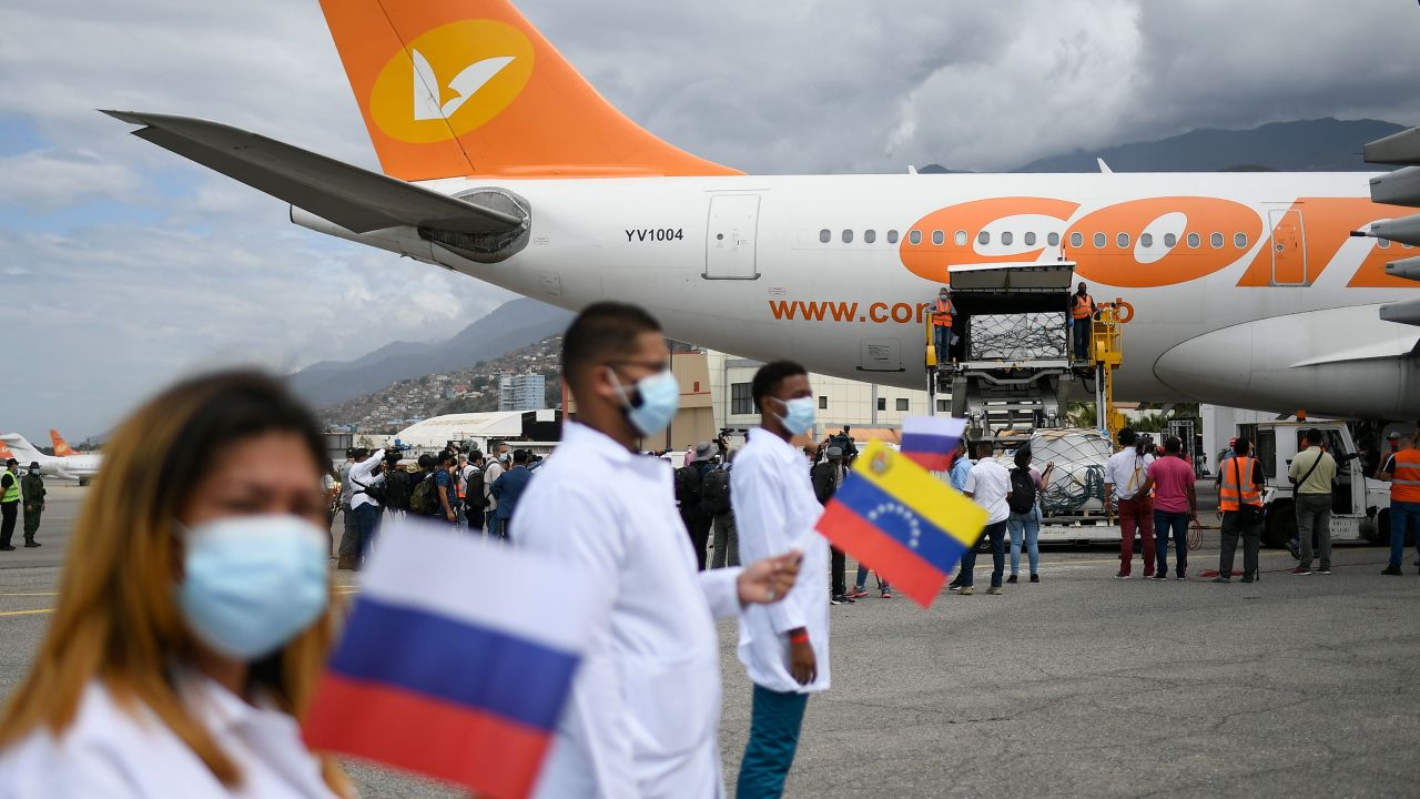 Healthcare workers hold national flags from Venezuela and Russia as workers unload a shipment of the Russian COVID-19 vaccine Sputnik V, at the Simon Bolivar International Airport in Maiquetia, Venezuela, Saturday, Feb. 13, 2021. 