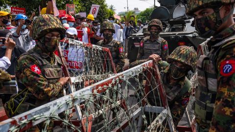 Protesters hold banners and shout slogans while Myanmar military soldiers from the 77th Light Infantry Division place barbed wire barricades on February 15, 2021 in Yangon, Myanmar. 