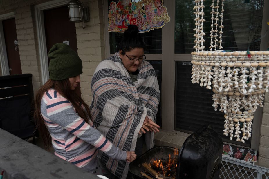 Karla Perez and Esperanza Gonzalez warm up by a barbecue grill after their power was knocked out in Houston on Tuesday.