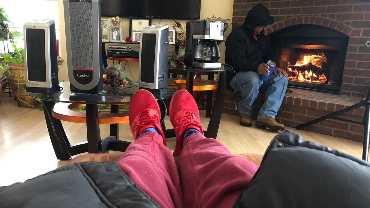 Eric Siner, Jr. warms his feet while his father sits by the fireplace after their neighbor hooked up their heaters to his generator.