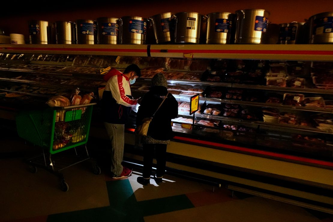 Customers use the light from a cell phone to look in the meat section of a grocery store in Dallas.