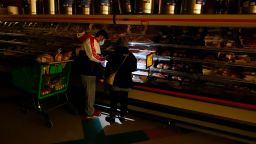 In this Feb. 16, 2021, file photo, customers use the light from a cell phone to look in the meat section of a grocery store in Dallas. Making decisions about risks — large or small — in the pandemic era is fraught enough. But the storms and outages ravaging Texas and other states have added a whole new layer to the process. (AP Photo/LM Otero)