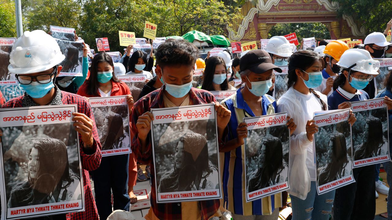 Mandalay University graduates bow their heads as they hold posters with images of Mya Thweh Thweh Khine on February 14, 2021.