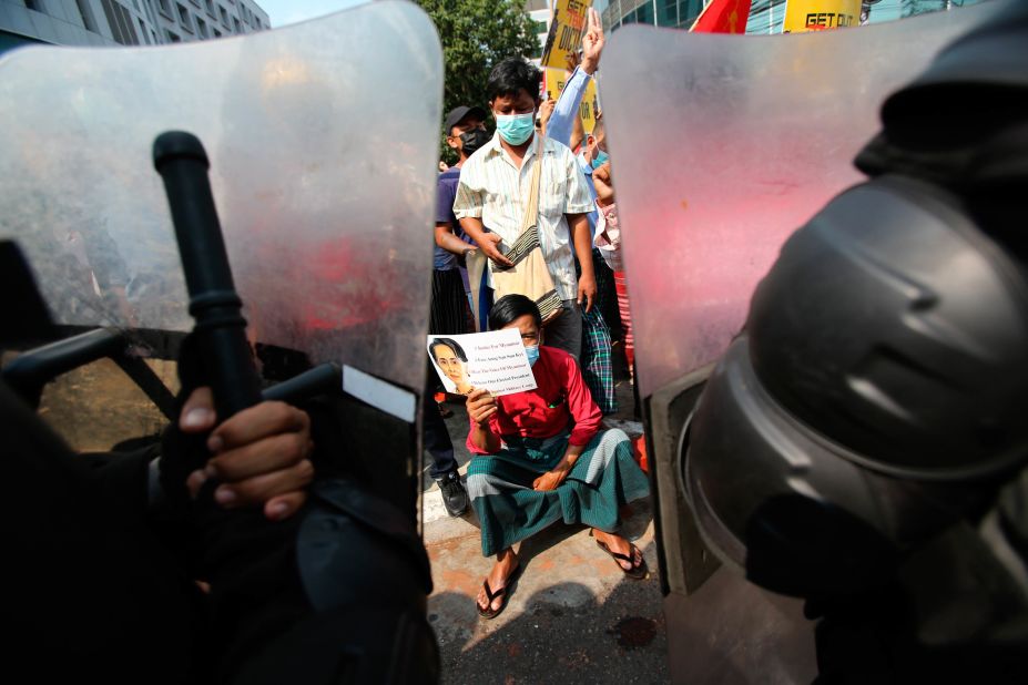 A protester holds a Suu Kyi poster as he sits in front of police in Yangon on February 19.