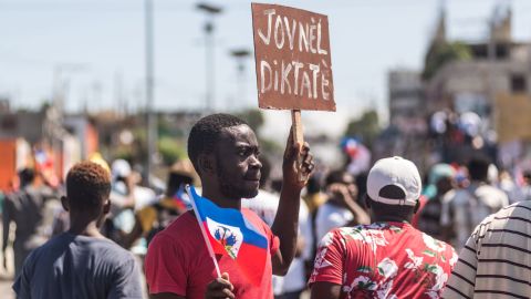 People hold up signs during a demonstration against the Moise government in Haiti's capital on February 14, 2021.