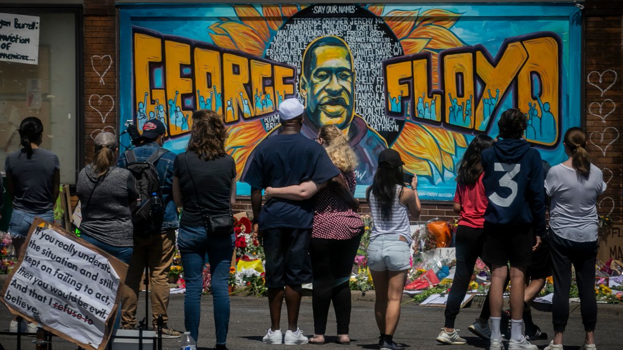 FILE - In this May 31, 2020 file photo, visitors make silent visits to organic memorial featuring a mural of George Floyd, near the spot where he died while in police custody, in Minneapolis, Minn. On Wednesday, Dec. 8, 2020, the Minneapolis City Council will decide whether to shrink the city's police department while violent crime is already soaring and redirect funding toward alternatives for reducing violence. (AP Photo/Bebeto Matthews, File)