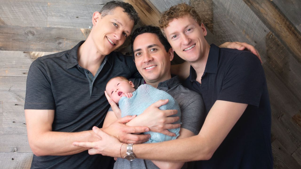 Ian Jenkins, left, with his partners Alan, center, and Jeremy. Alan is holding their daughter Piper.