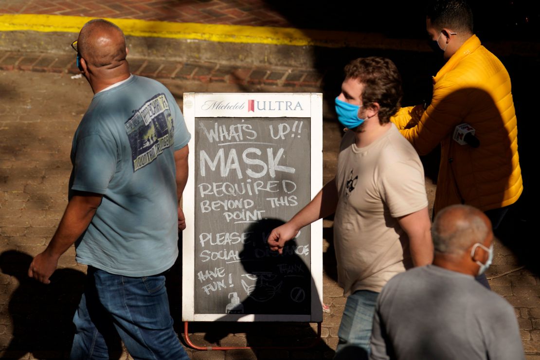 Visitors wearing face masks walk past a sign requiring masks at a restaurant along the River Walk, Wednesday, March 3, 2021, in San Antonio.