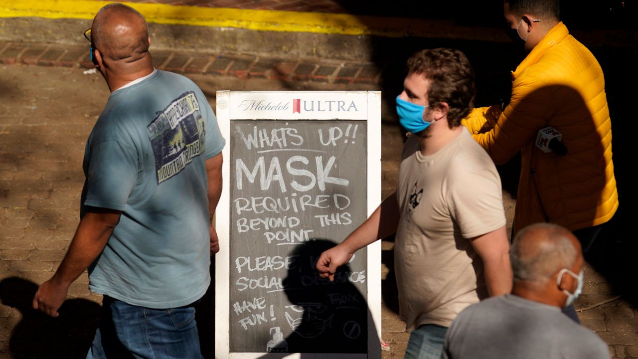 Visitors wearing face masks walk past a sign requiring masks at a restaurant along the River Walk, Wednesday, March 3, 2021, in San Antonio. 