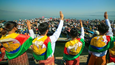 Protesters wearing traditional Shan dress make the three-figner salute as others hold signs during a demonstration against the Myanmar military coup in Inle lake, Shan state on February 11.