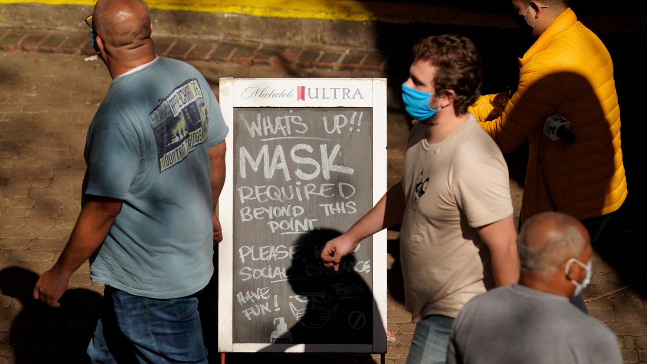 People wearing face masks walk past a sign requiring masks at a restaurant along the River Walk in San Antonio, Texas.