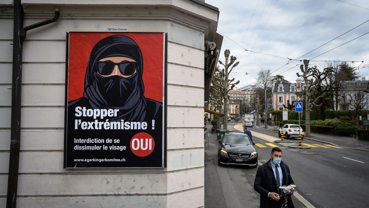 A man wearing a face mask walks on February 4, 2021 in Lausanne past an electoral poster in favor of a "burqa ban" initiative reading in French: "Stop extremism!"