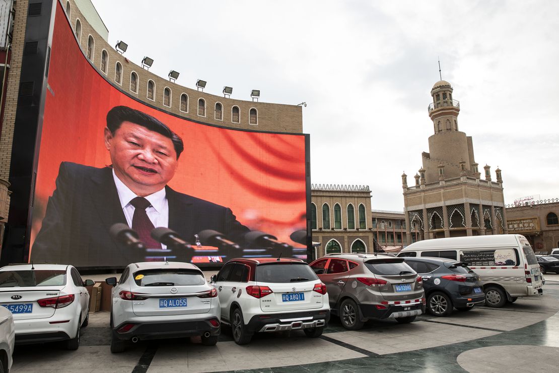 Vehicles stand in a parking lot as a large screen shows an image of Chinese President Xi Jinping in Kashgar, Xinjiang autonomous region, China, on Thursday, November 8, 2018.