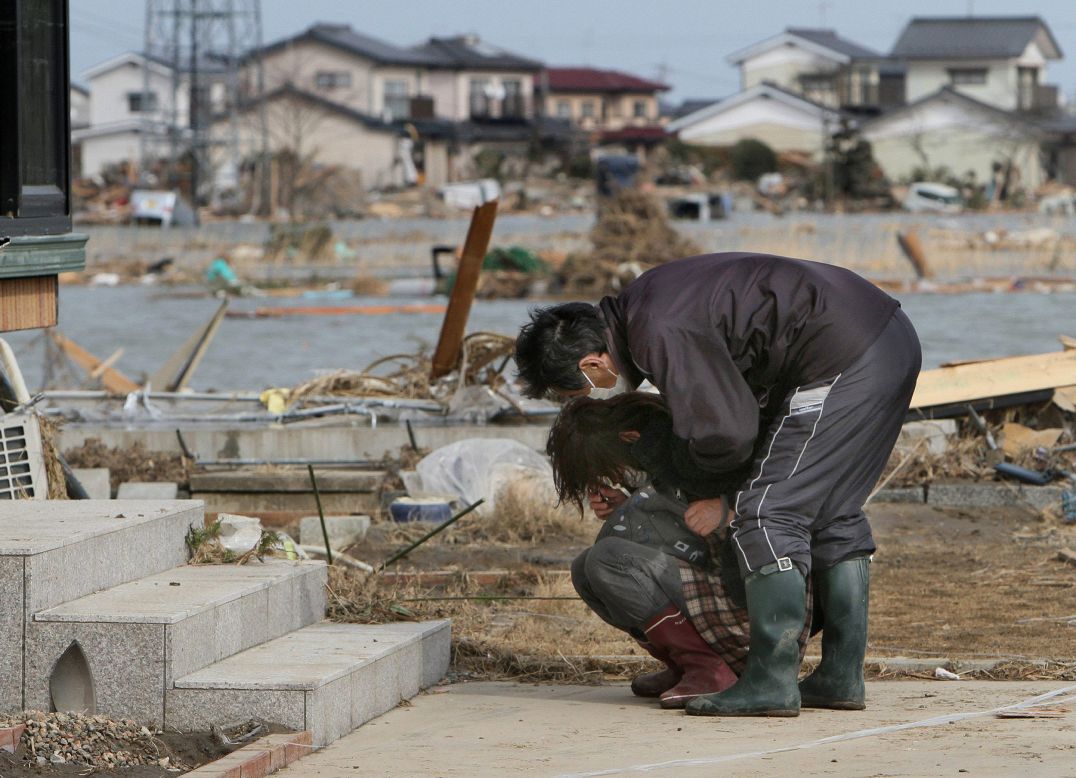 A man comforts a woman as she cries in front of her damaged home in the town of Watari in Miyagi prefecture.