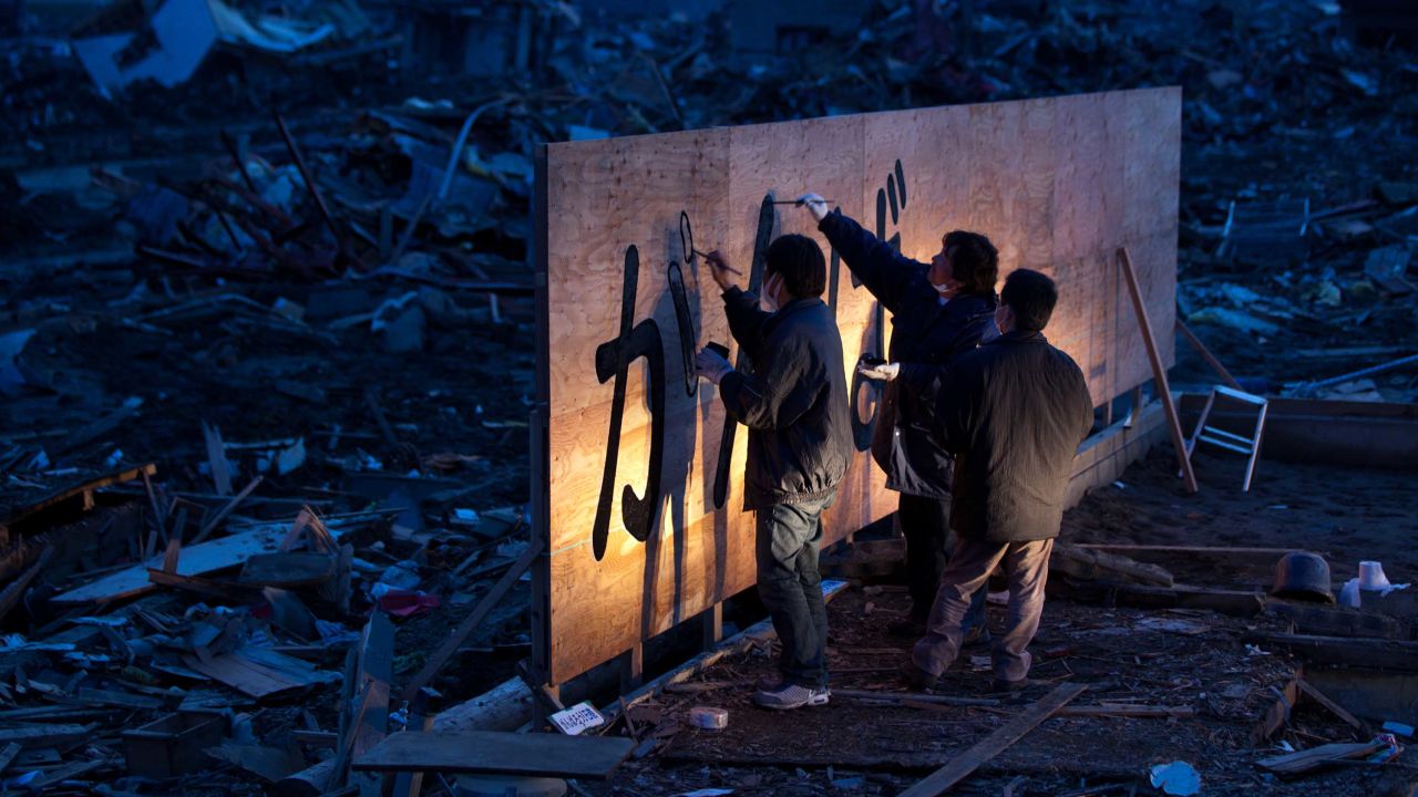 Kenichi Kurosawa (center) and his friends draw the words "Ganbaro!" or "hang in there" on a billboard lit up with car headlights in Ishinomaki, Miyagi prefecture on April 10, 2011.
