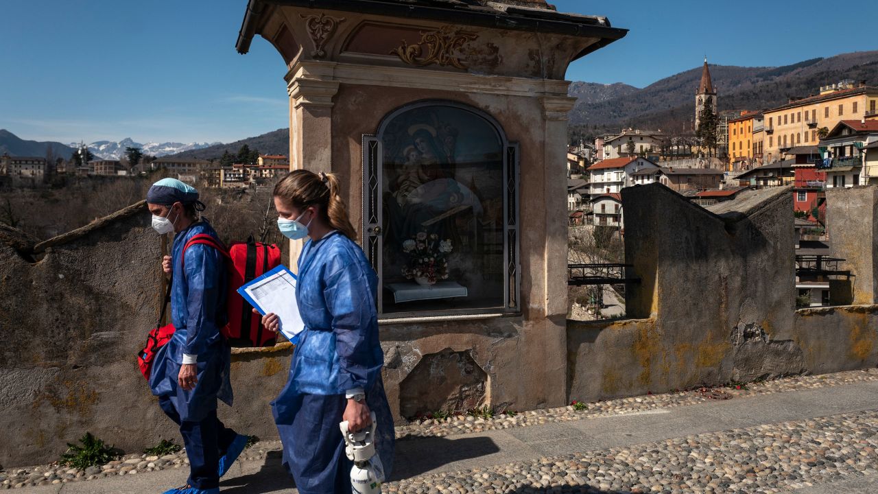 Medical workers walk on the "Ponte del Diavolo" (Devil's Bridge) on March 13, 2021 in Dronero, Maira Valley, near Cuneo, northwestern Italy during a home vaccination campaign with the Moderna Covid-19 vaccine for elderly residents.