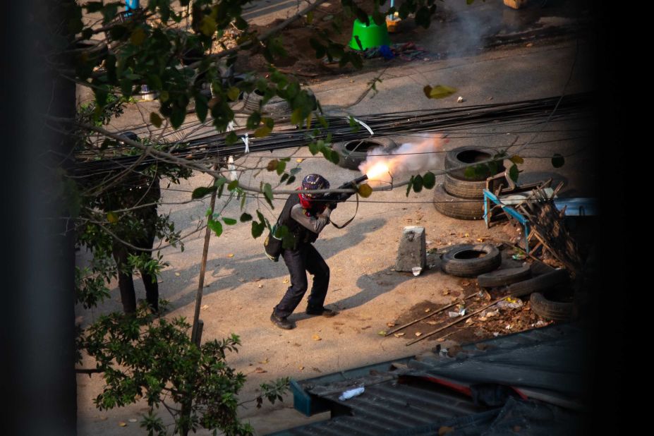 A member of Myanmar's police is seen firing a weapon toward protesters in Yangon on March 13.
