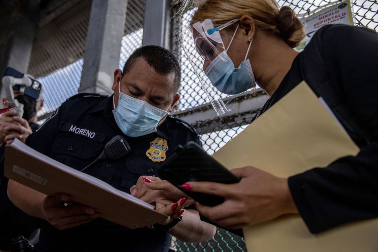  A US Customs and Border Protection officer checks for the name of a migrant as a group of at least 25 asylum seekers were allowed to travel from a migrant camp in Mexico into the United States on February 25. The group was the first allowed to cross into south Texas as part of the unwinding of the Trump administration's Migrant Protection Protocols. Many of the asylum seekers had been waiting in a squalid camp alongside the Rio Grande for more than a year.