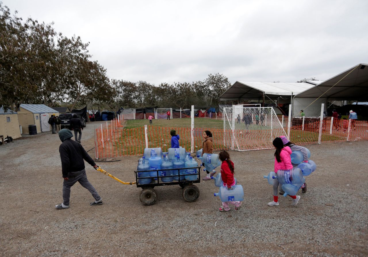 Migrants seeking asylum in the United States carry empty water jugs at a camp in Matamoros, Mexico, on February 18.