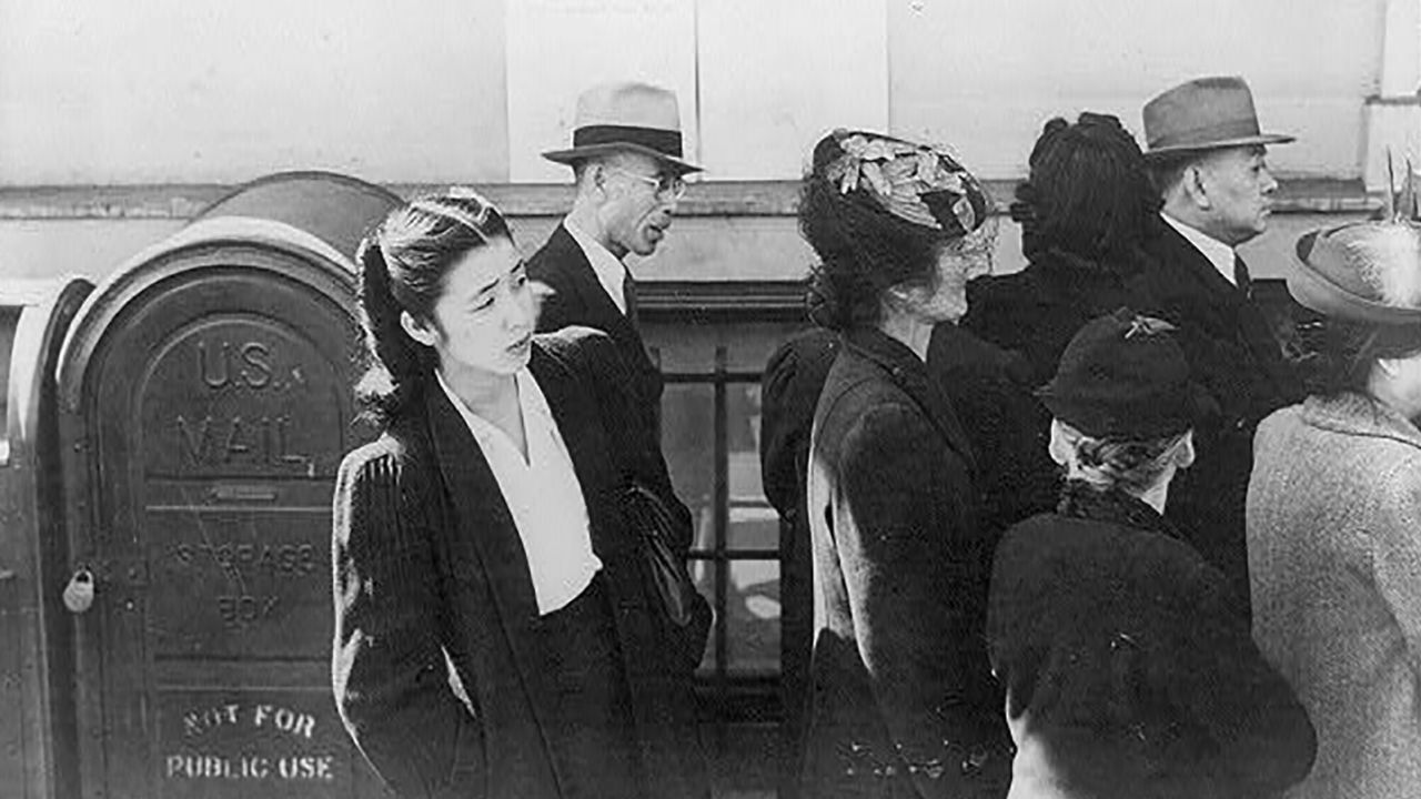 Shizuko Ina standing behind others waiting to be assigned a "family number" before being removed from their homes and incarcerated in a detention facility at Tanforan Racetrack.