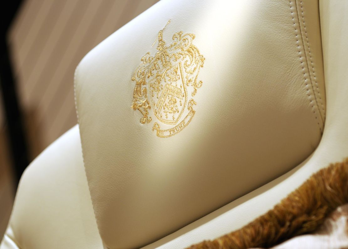 A gold-threaded, embroidered Trump family crest on the headrest of a chair