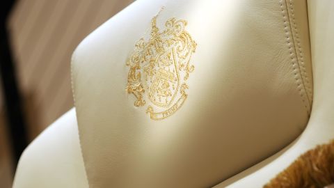 A gold-threaded, embroidered Trump family crest on the headrest of a chair