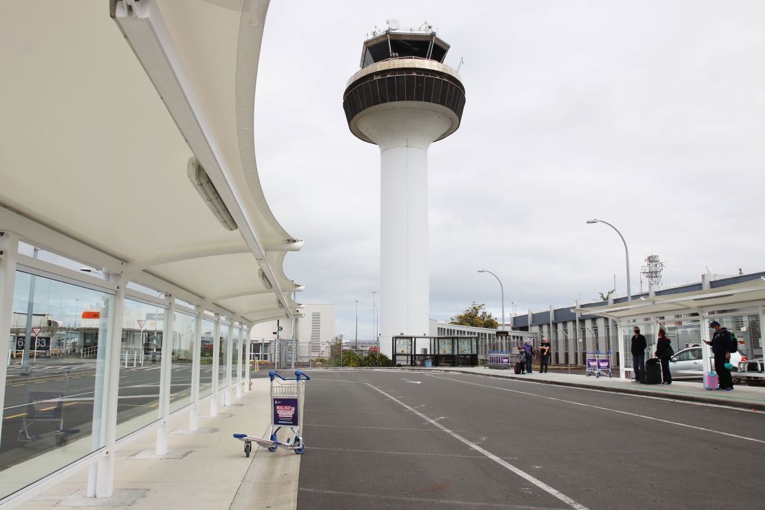 AUCKLAND, NEW ZEALAND:  A small group of passengers wait for shuttle buses below the air traffic control tower after arriving at Auckland Domestic Airport on 7 October 2020, two days before the lifting of Alert Level 2 restrictions for the Auckland region that were put in place following the re-emergence of Covid-19 in the community (Photo by Lynn Grieveson - Newsroom via Getty Images)
