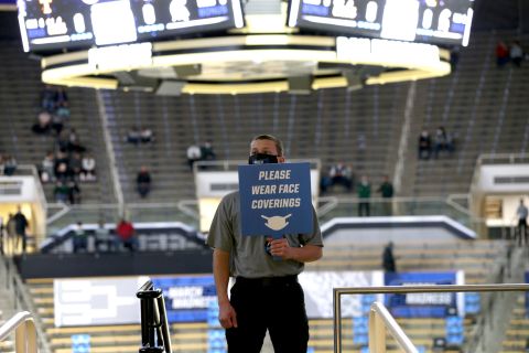 A worker holds a sign encouraging spectators to wear masks before the Michigan State-UCLA game.