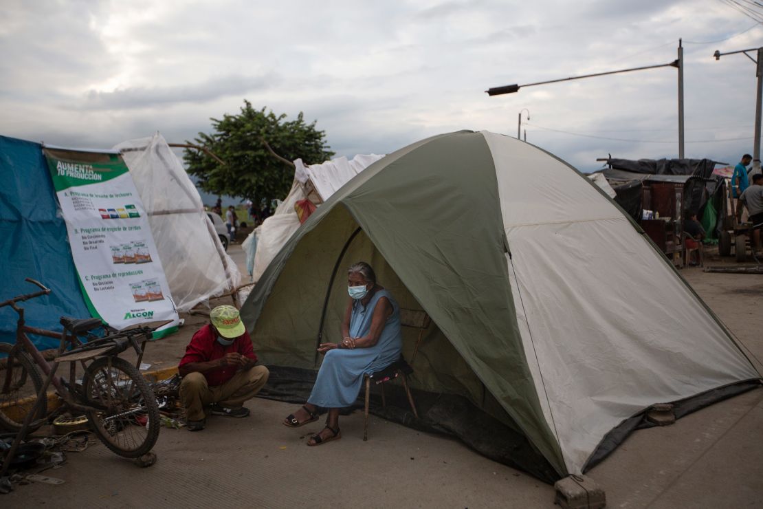An elderly woman sits outside a tent in Lima, Honduras, where she lives after losing her home in last year's hurricanes Eta and Iota. Devastation from the storms and the economic damage of the Covid-19 pandemic have added to the forces that drive Hondurans to migrate.