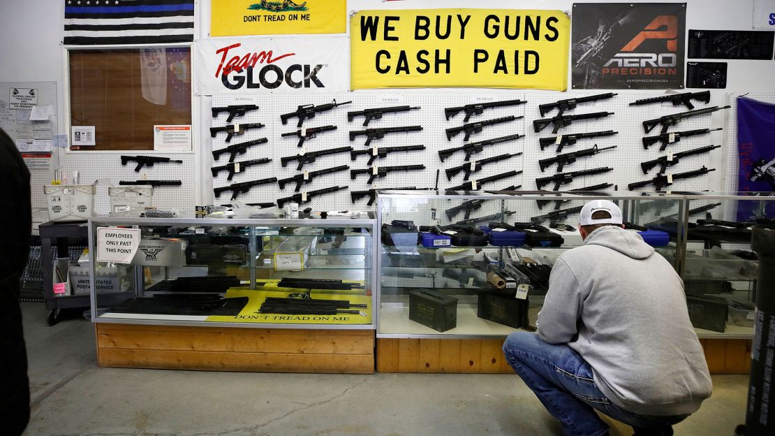 A customer looks at handguns in a case as AR-15 style rifles hang on a wall at Davidson Defense in Orem, Utah on February 4, 2021.